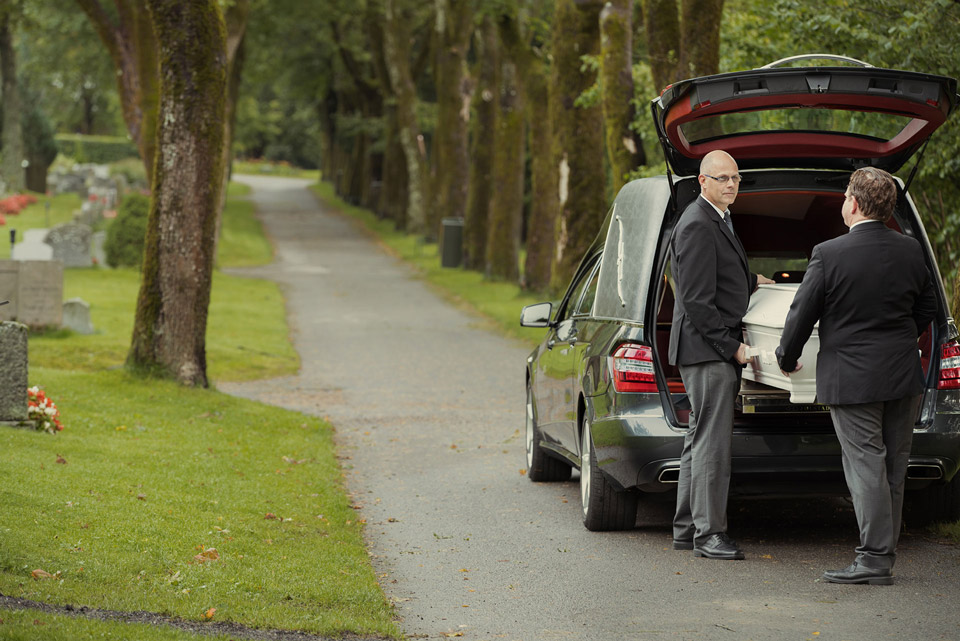 Kiste bæres ut fra begravelsesbil av grevferdskonsulenter fra Jølstad begravelsesbyrå